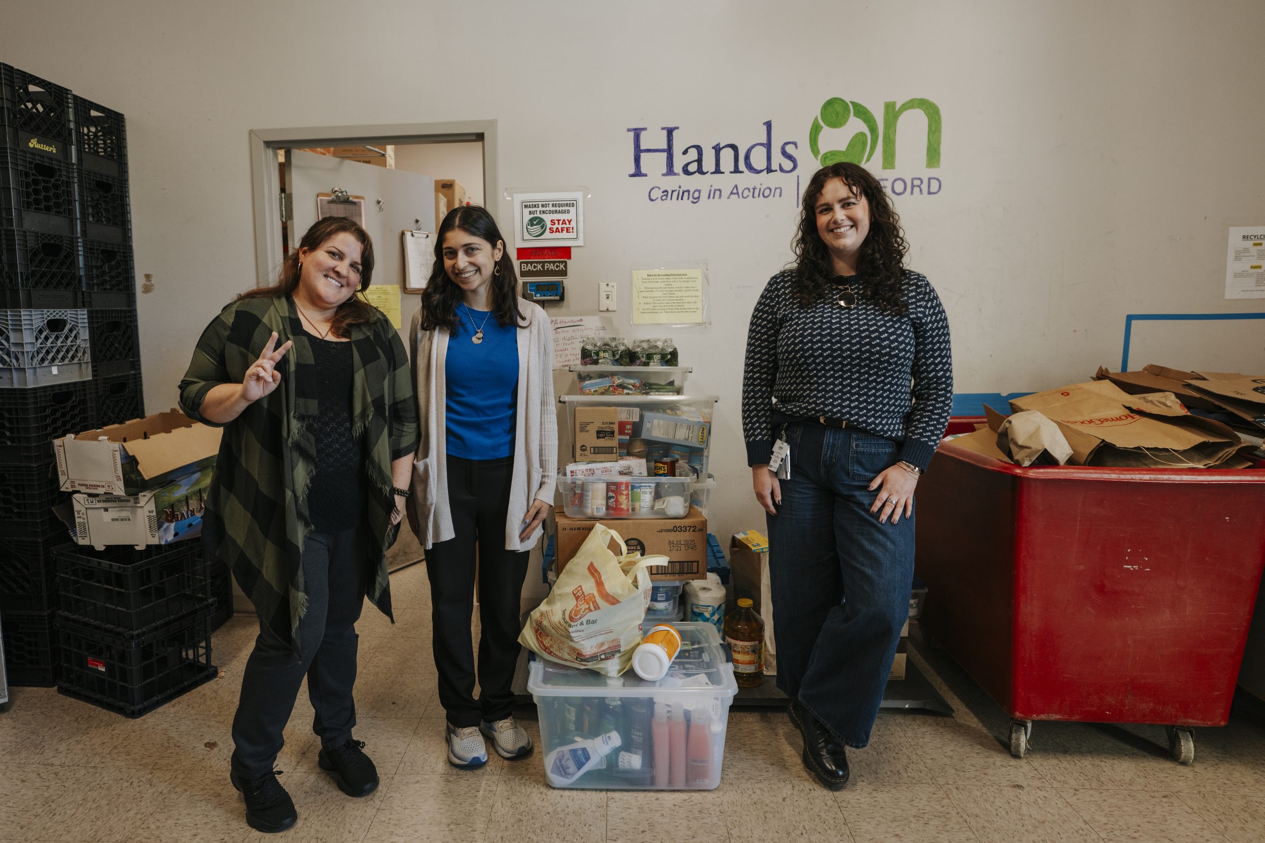 Kelly Dougherty, the organization’s Community Engagement and Partnerships & Communications Coordinator, & GA's Taline Norisgian, and Julia Szcech stand next to cart with donated items
